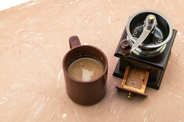 a cup of coffee and a coffee grinder on a beige copyspace surface