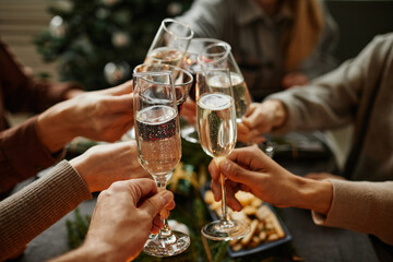 Close up of friends clinking champagne glasses while enjoying Christmas dinner together sitting by...