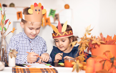 Girl and boy in paper turkey and native American hats writing I am thankful for. Celebrating...