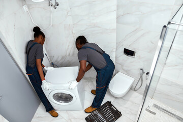 Young man and woman moving washing machine, high angle