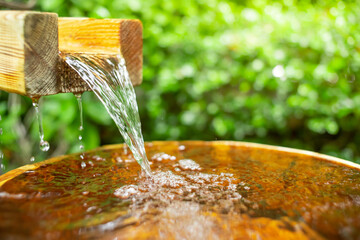 Water from the natural hot springs flows into the wooden bucket. soft focus.green tree background