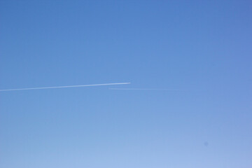 Two planes fly towards each other. Inversion trail of clouds from the plane against the blue sky. Airplane leaving vapor trail behind. Track in the sky from a jet plane.