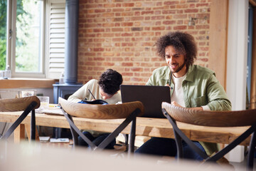 Fototapeta premium Father using laptop with son doing homework