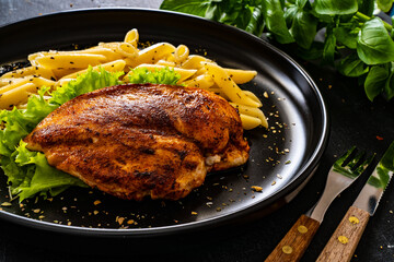 Fried chicken breast with pasta and vegetables on wooden background
