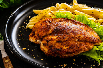 Fried chicken breast with pasta and vegetables on wooden background
