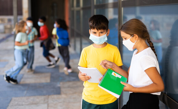 Portrait of primary school girl and boy wearing protective face masks talking outside before lesson, new normal during coronavirus pandemic situation