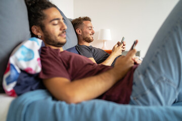 gay couple using smartphone digital devices lying on the bed. Homosexual couple watching social...