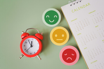 top view of red analog alarm clock , facial emotional and blurred yearly calendar on green background