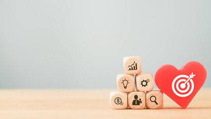 white dartboard icon on red heart and pyramid of business icon cubes on wood for brainstorming, target and goal of business concept