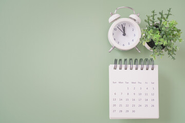top view of analog alarm clock ,calendar and small fake tree on green background with copy space