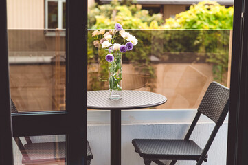 A bouquet of flowers is on the table on the terrace. There are chairs on the sides of the table.
