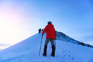 Fototapeta na wymiar Mountaineer reaches the top of a snowy mountain in a sunny winter day