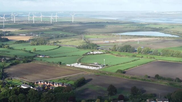 Cheshire farmland countryside wind farm turbines generating renewable green energy aerial pan right reveal view