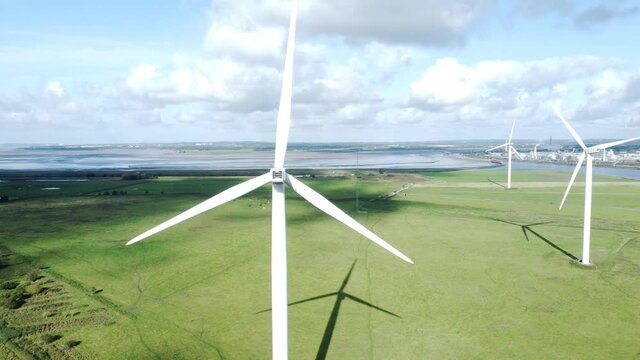 Alternative green energy wind farm turbines spinning in sunny Frodsham Cheshire fields aerial view rising left