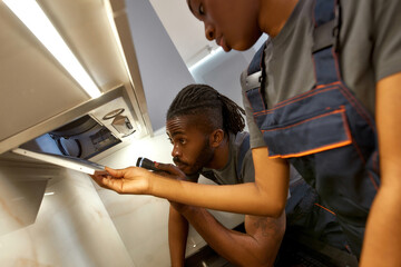 Female assistant helping professional electrician to troubleshoot kitchen hood