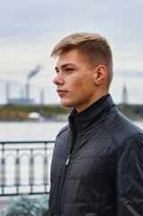 One handsome young man on the city river embankment in a black leather jacket. In the background in...
