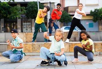 International group of modern tweenagers performing street dance choreography outdoors in summer.