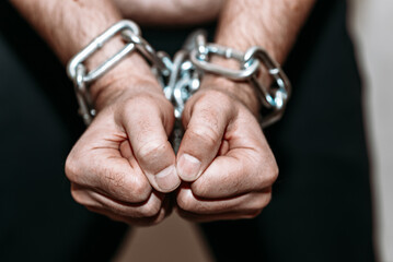 Repented man prisoner with his hands shackled in chains on a dark gray background.Closeup.