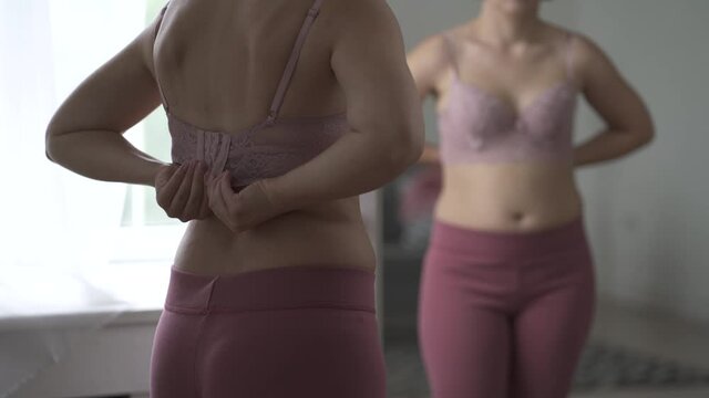 A woman tries on a bra in the fitting room, a bustier with a wide clasp is reflected in the mirror, close-up 4k video