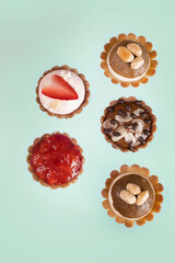 Raw vegan cupcakes with strawberry, nuts, chocolate, cashew cream and caramel on mint background. Top view.