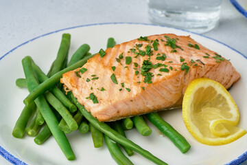 Closeup of juicy and flavorful baked salmon fillet with asparagus, lemon slice and parsley in extra-virgin olive oil. Incredible healthy and tasty meal. Omega3 fish. Seafood lunch. Horizontal