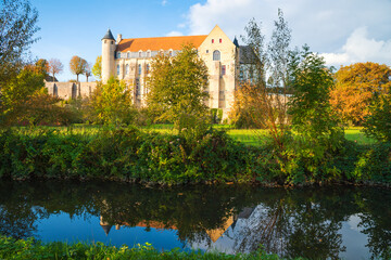 Ancient Saint Severin abbey building (nowadays nursing home) and its reflection in water. Chateau-Landon, France. Autumn travel in French countryside.