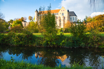 Medieval landscape. Ancient Saint Severin abbey building and its reflection in water. Chateau-Landon, France. Autumn travel in French countryside.