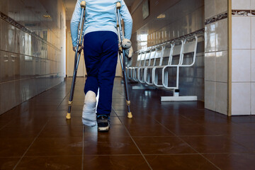 Child walks along hospital corridor on crutches to see doctor. Girl has one leg broken in cast.