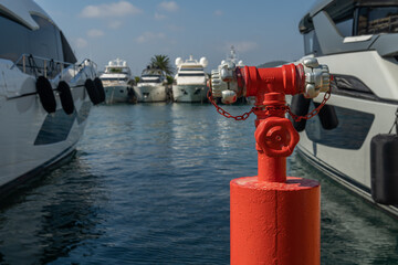 Close-up of a fire hydrant and out of focus in the background, a marina with luxury yachts moored....