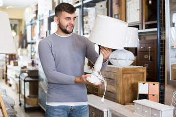 Happy man choosing vintage table lamp in shop of secondhand furniture