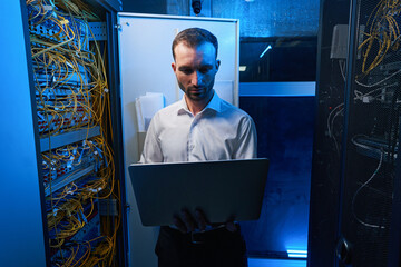 Man using laptop near open server cabinet