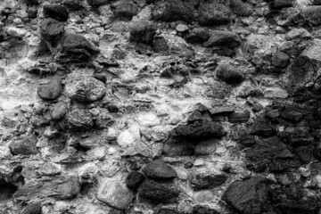 old weather damaged medieval castle wall made of field stones. Black and white background