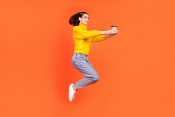 Fototapeta na wymiar Full body profile side photo of young woman happy positive smile give cup of coffee jump up isolated over orange color background