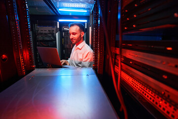 Data center system administrator checking server settings with laptop
