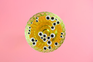 artificial eyes in a glass with a green drink on a pink background. Halloween party decorations