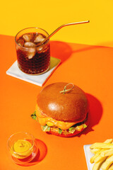 Big burger with french fries and sauce on bright orange and yellow background. American Fast food cuisine in retro style. Copy space