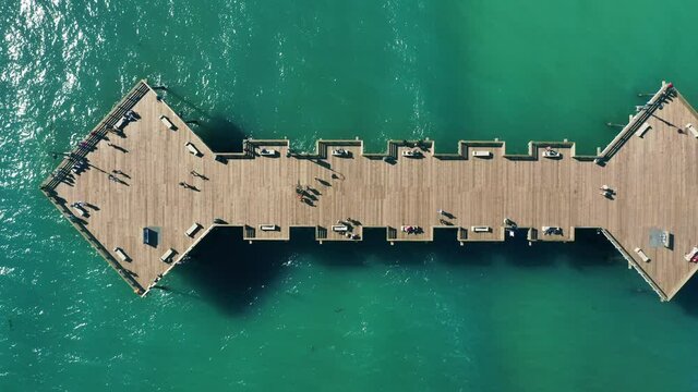 Cinematic top down view on scenic pier at Pismo Beach, California USA. Perfect summer background with copy and text space on green blue ocean with people walking by the pier on sunny summer day 4K