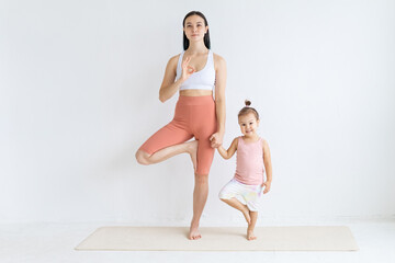 Fototapeta na wymiar Young woman practices yoga with her daughter. Children's yoga. Vrikshasana pose.