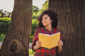 Fototapeta premium Portrait of attractive cheerful dreamy carefree girl wearing checked shirt reading diary spending free time on fresh air outdoors