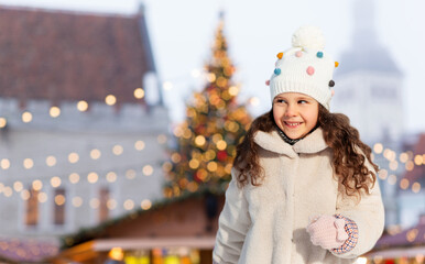 winter holidays and children concept - portrait of happy little girl over christmas market at old...
