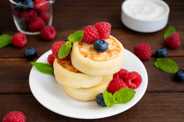 Cottage cheese pancakes with fresh berries, sour cream and honey on a dark wooden background. Homemade traditional Ukrainian and Russian syrniki.