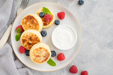 Cottage cheese pancakes with fresh berries, sour cream and honey on a gray concrete background. Homemade traditional Ukrainian and Russian syrniki.