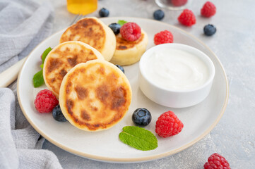 Cottage cheese pancakes with fresh berries, sour cream and honey on a gray concrete background. Homemade traditional Ukrainian and Russian syrniki.