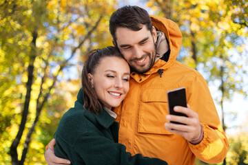 technology, season and people concept - happy couple with smartphone over autumn park background