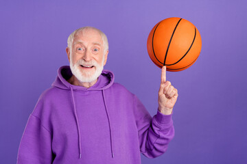 Portrait of attractive cheerful man spinning on forefinger ball active hobby isolated over bright violet purple color background