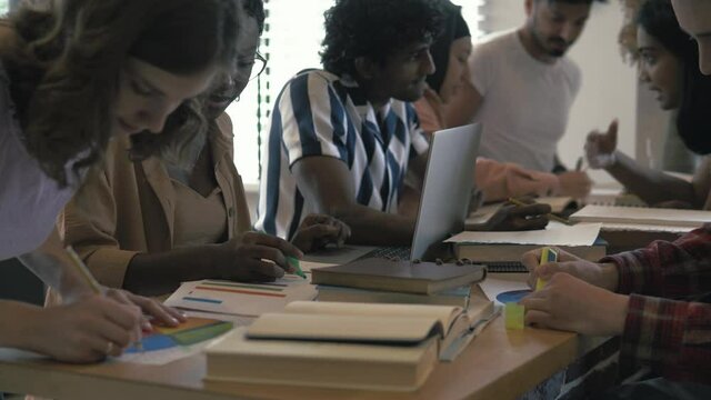 Focused diverse college university students team study together using laptop prepare for exam in library, multiethnic young people group talk looking at computer do online research project assignment