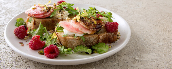 a plate of bruschettas with cream cheese, peaches and raspberries on a light table