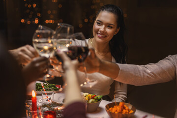 holidays, party and celebration concept - multiethnic group of happy friends having christmas dinner at home and drinking wine