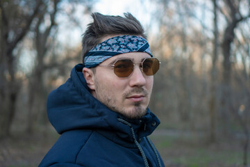 Portrait of a young and stylish man in sunglasses and a bandana. Male model showing fashion. Style concept.