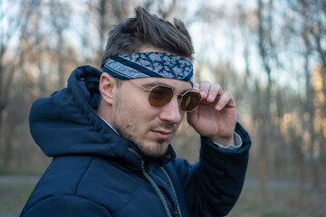 Portrait of a young and stylish man in sunglasses and a bandana. Male model showing fashion. Style concept.